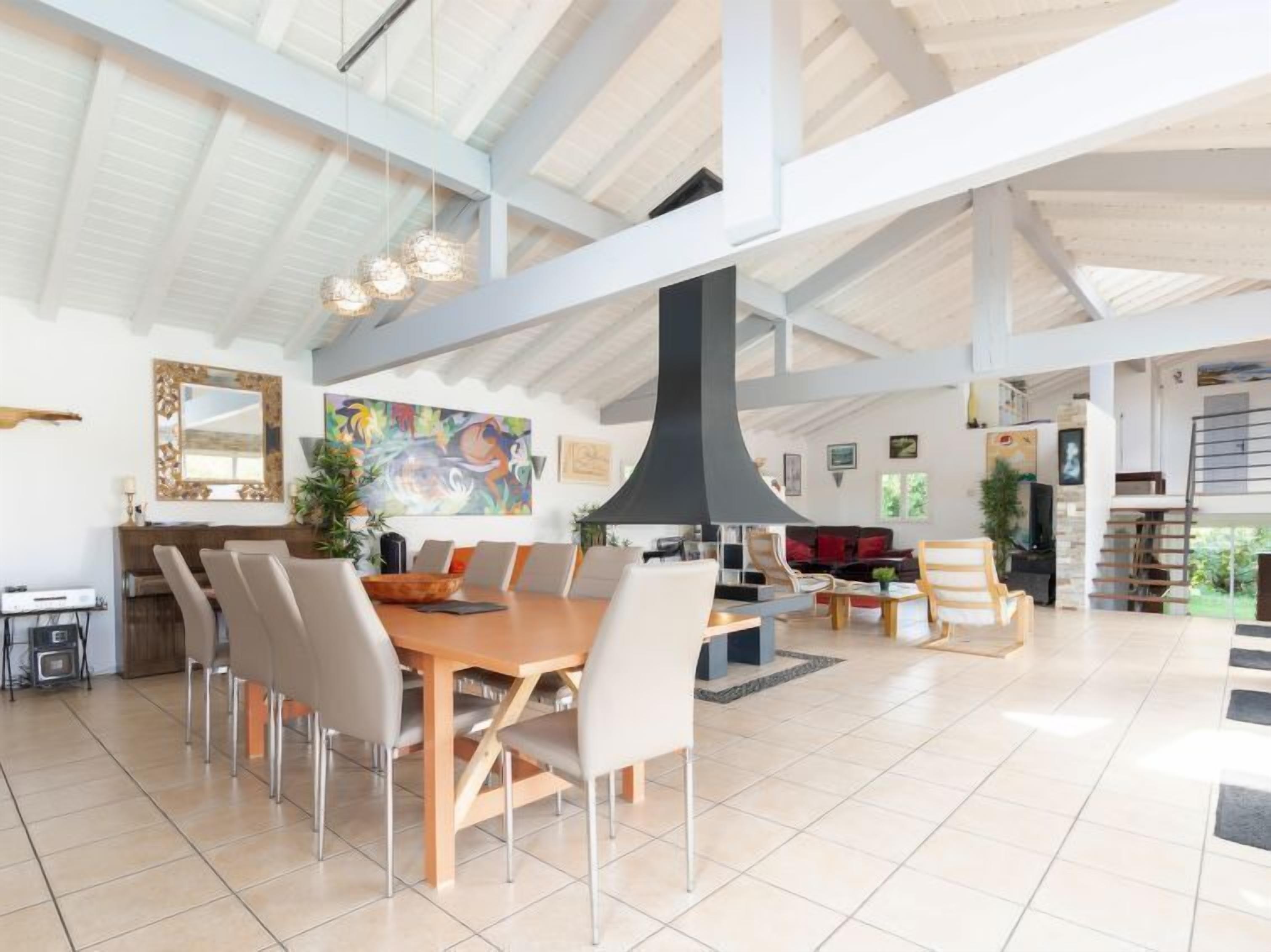 Een ruime woonkamer met een hoge plafond, een eettafel met stoelen, een open haard en een groot schilderij aan de muur.
