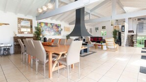 Een ruime woonkamer met een hoge plafond, een eettafel met stoelen, een open haard en een groot schilderij aan de muur.