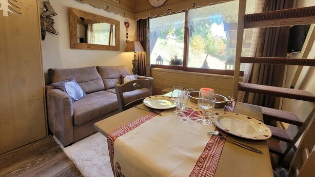 A cozy room with a wooden interior, a dining table set with plates and glasses, a sofa, and a chandelier.