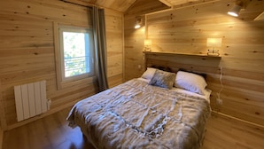 A wooden cabin bedroom with a bed, bedside lamps, a window, and a radiator.