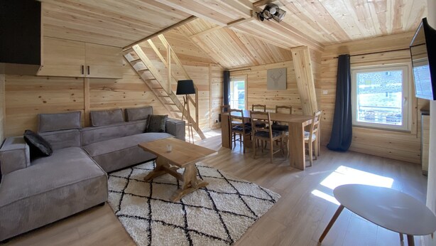 A cozy cabin interior with a sofa, dining table, chairs, and a ceiling fan.