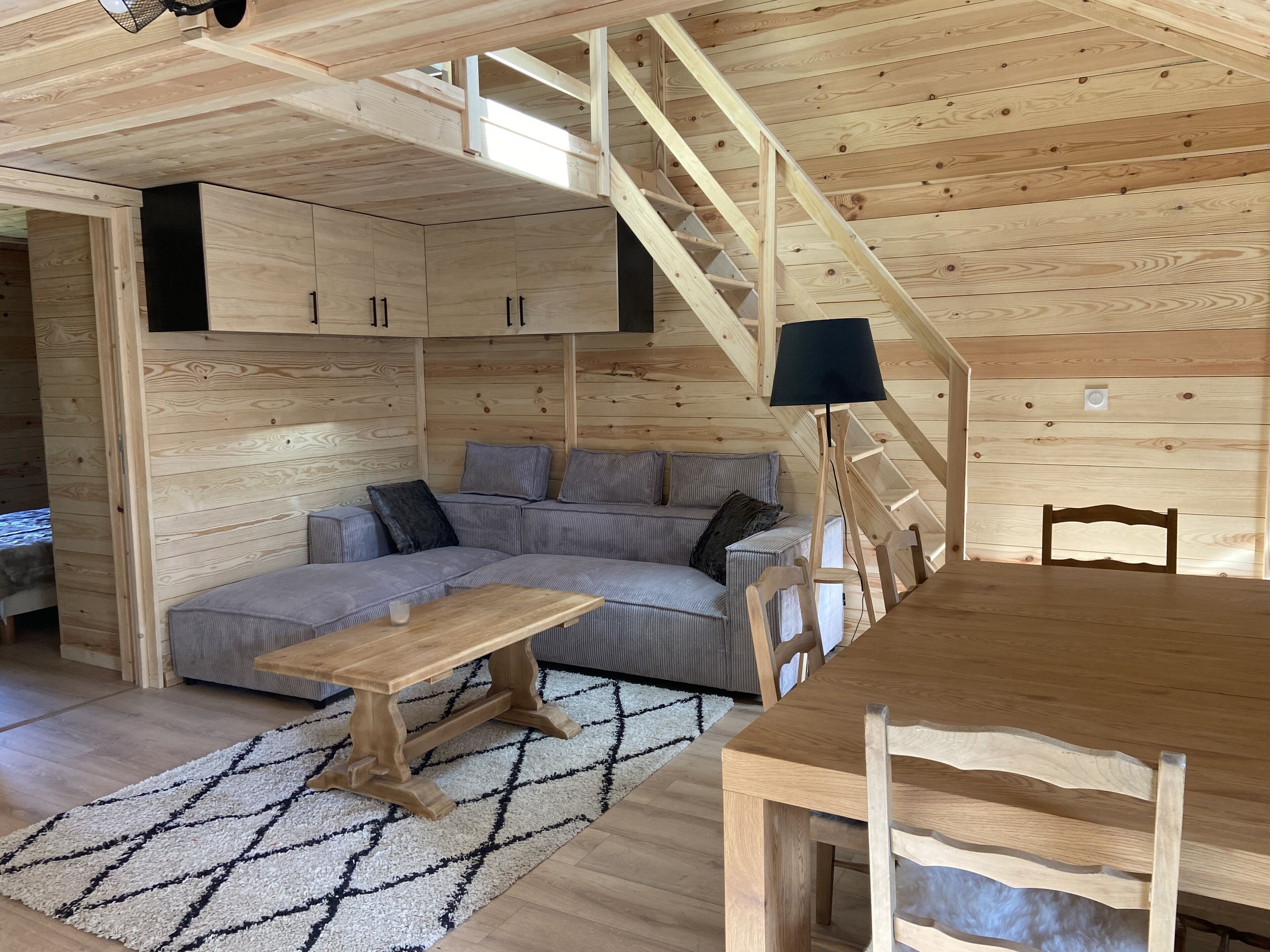Interior acogedor de una cabaña con una escalera de madera, un sofá, una mesa de comedor y una lámpara.