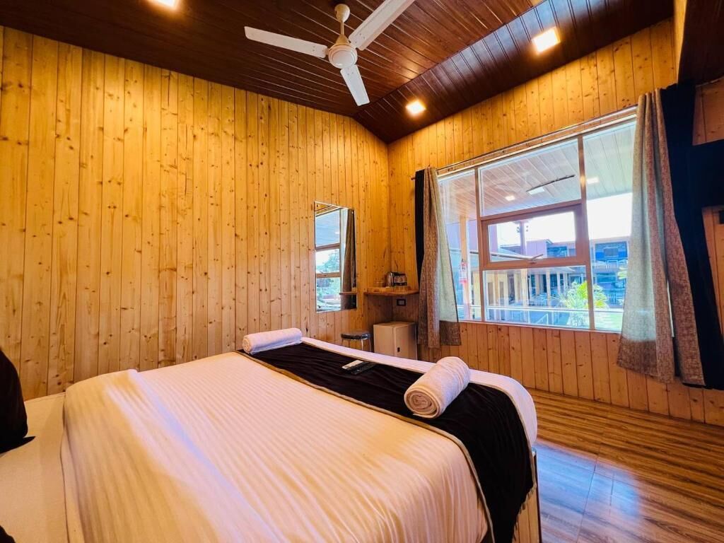 A wooden-paneled room with a bed, a ceiling fan, and a window with curtains.