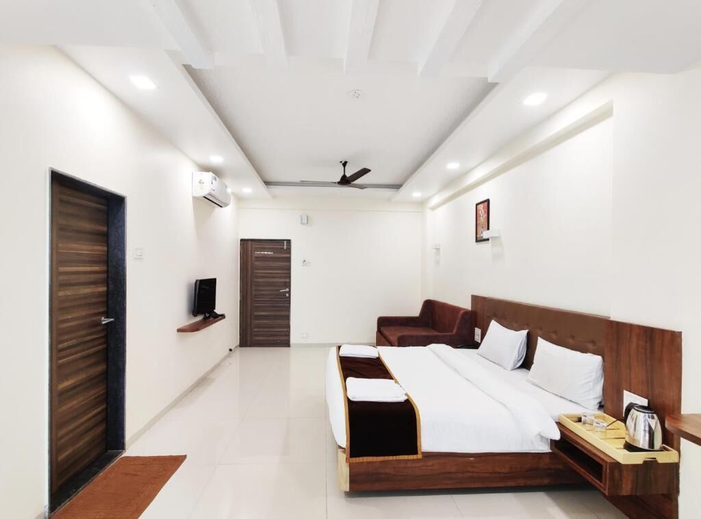 A modern hotel room with a wooden bed, a TV, a bedside table with a kettle, and a door with a wooden panel.