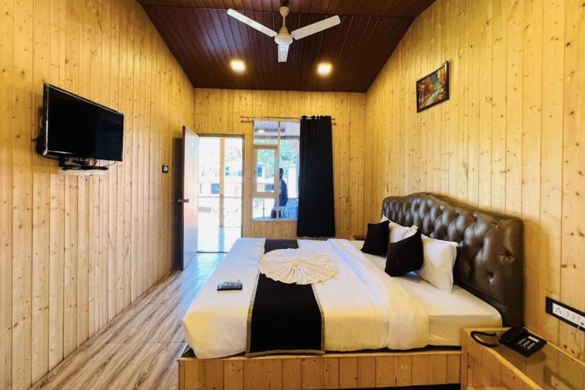A wooden-paneled room with a bed, a ceiling fan, a TV, and a door leading outside.