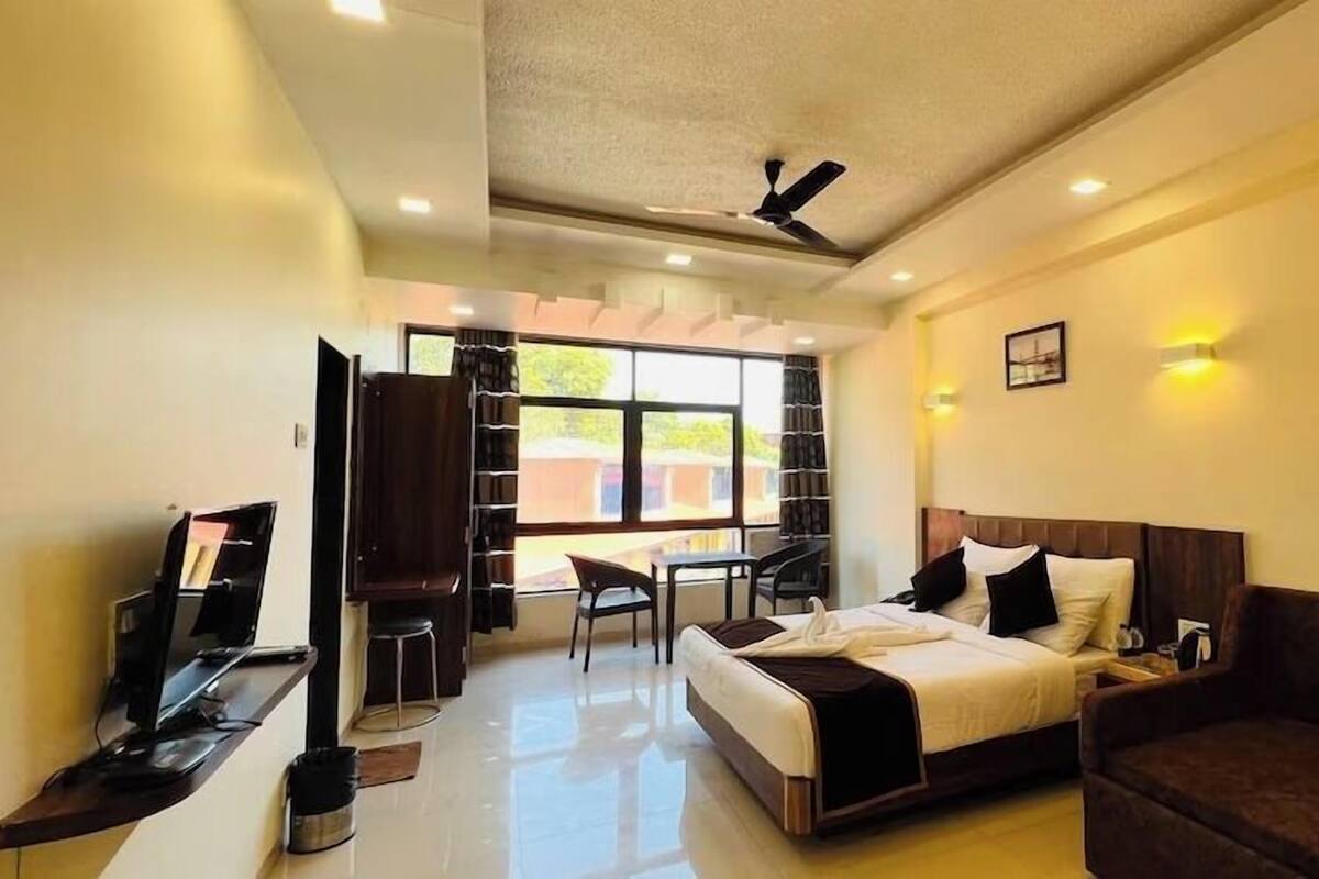 A hotel room with a bed, a sofa, a desk with a chair, and a bookshelf.