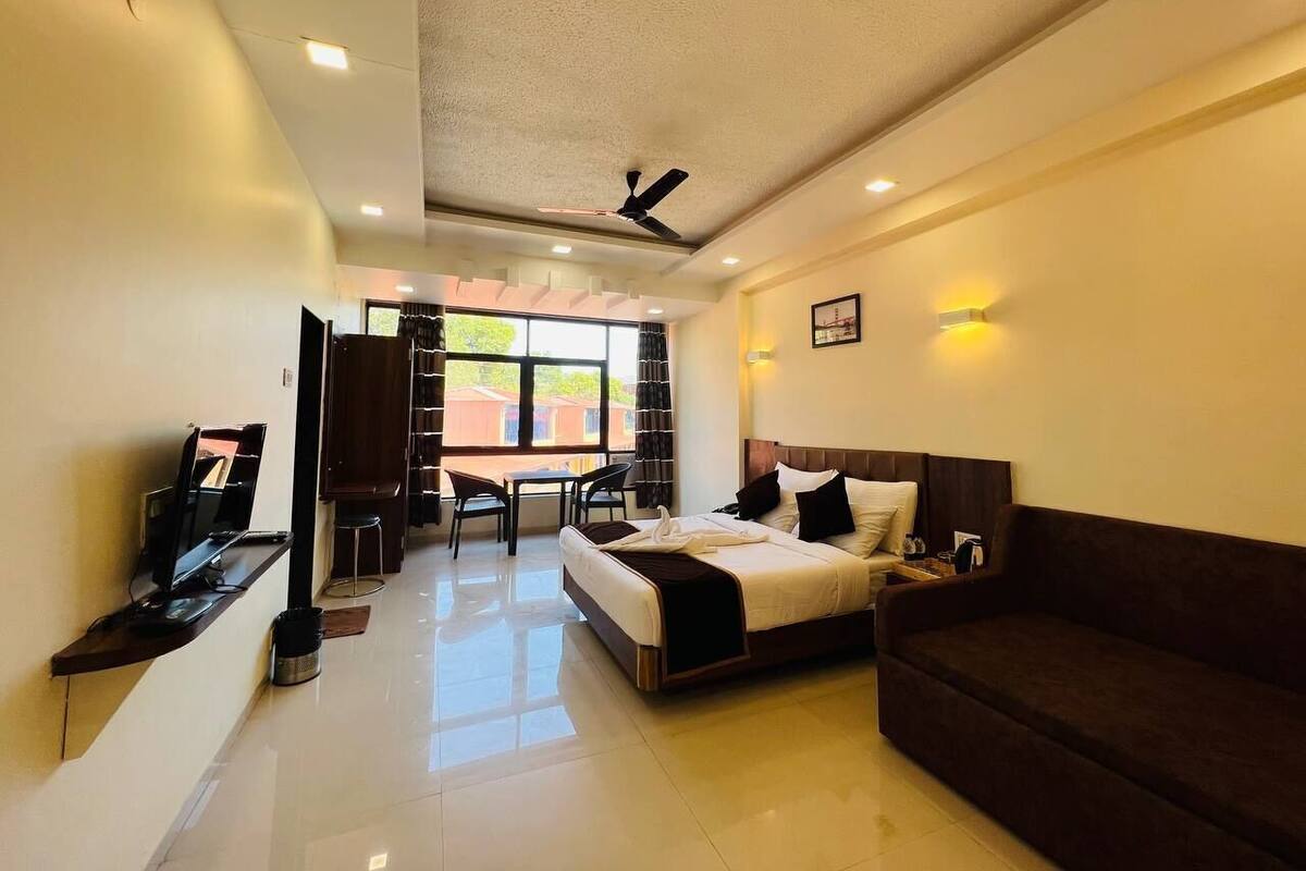 A hotel room with a bed, a sofa, a desk with a computer, a chair, and a window with a view.