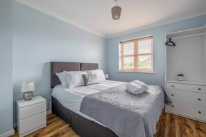 A bedroom with a bed, bedside table, dresser, and window with blinds.