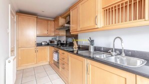 A kitchen with wooden cabinets, a black countertop, stainless steel sink, and a microwave. - 2 Bed Apt| Parking| Central Windsor By Tempstay (Windsor)