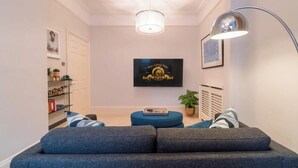 A modern living room with a sofa, a side table, a floor lamp, a television, and a framed picture on the wall. - Charming Character Home| 1 Bed| By Tempstay (Windsor)