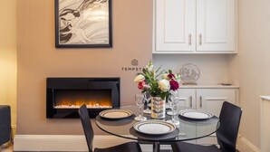 A dining area with a fireplace, a framed artwork, and a table set for two. - Charming Character Home| 1 Bed| By Tempstay (Windsor)