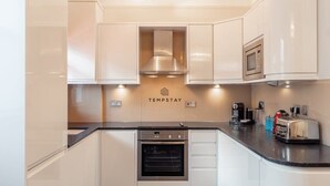 A modern kitchen with white cabinets, a built-in oven, a microwave, and a toaster on the countertop. - Charming Character Home| 1 Bed| By Tempstay (Windsor)