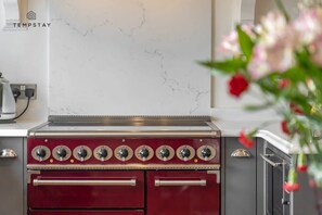A kitchen with a red stove, a marble backsplash, and a flower arrangement.