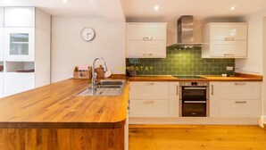 Una cocina moderna con armarios blancos, encimera de madera y salpicadero de azulejos verdes.