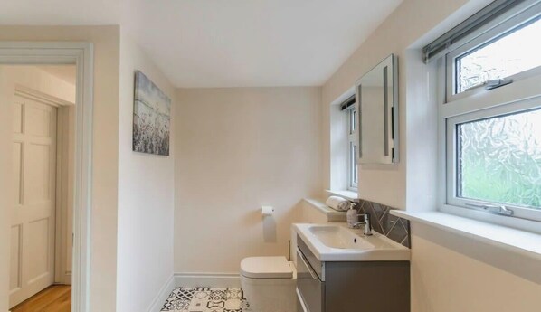 A bathroom with a toilet, sink, and window. - Modern Windsor 4 Bed Home W/ Parking - By Tempstay (Windsor)