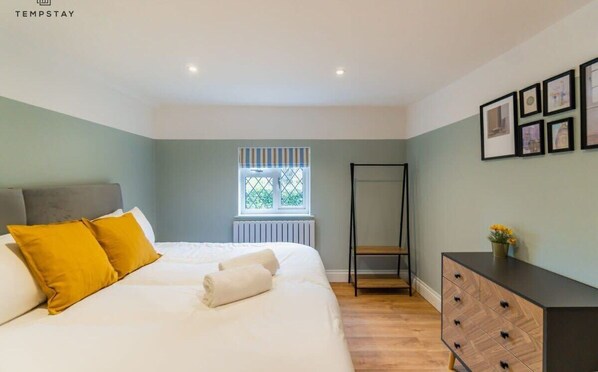A bedroom with a bed, a bench, a dresser, and a window with a view. - Modern Windsor 4 Bed Home W/ Parking - By Tempstay (Windsor)