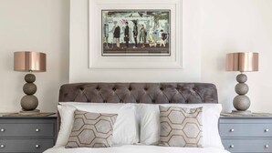 A bedroom with a tufted headboard, two bedside tables with lamps, a framed artwork above the bed, and a bed with patterned pillows. - Stunning Victorian Cottage in Windsor By Tempstay (Windsor)