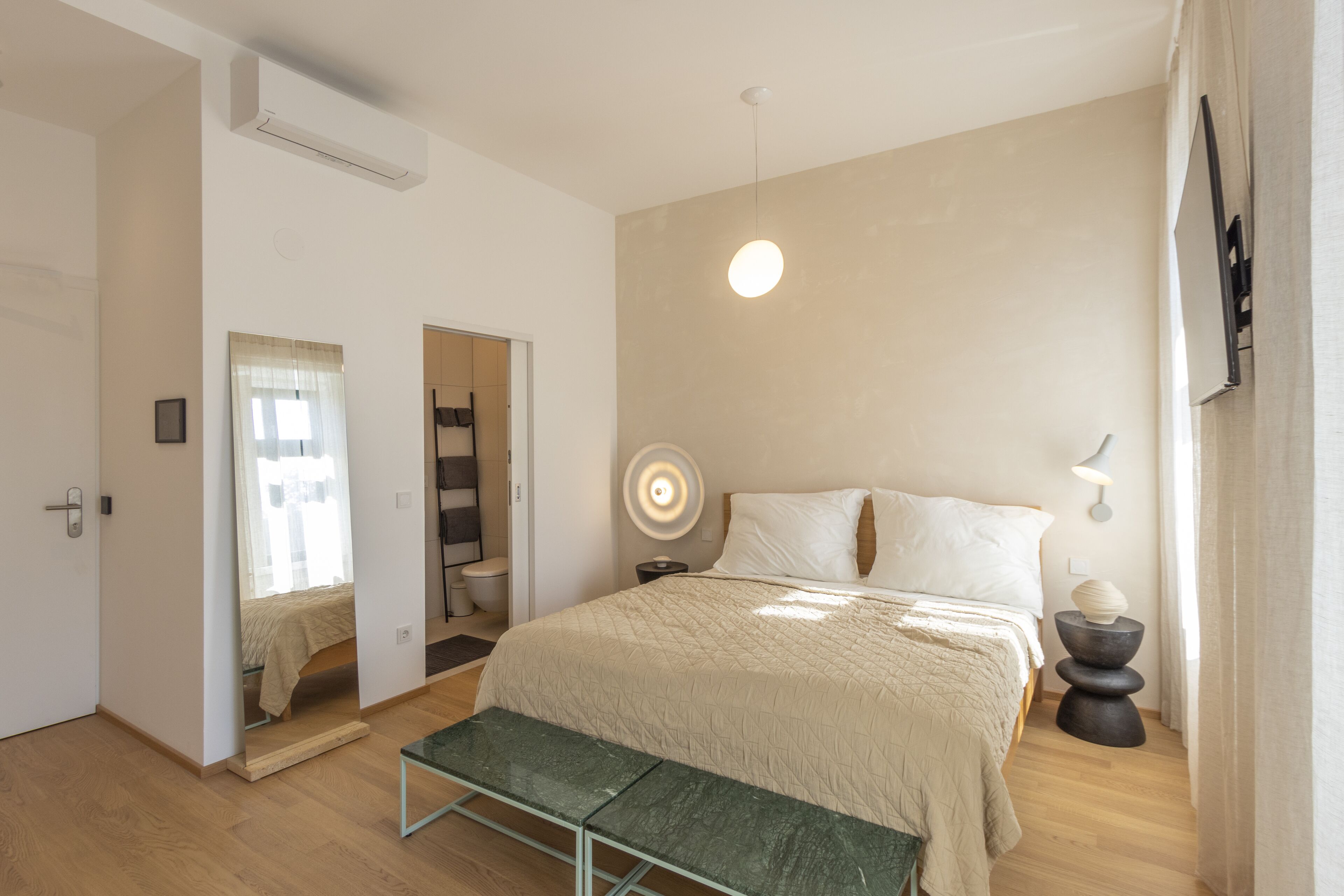 A bedroom with a bed, bedside table, lamp, and a bench.