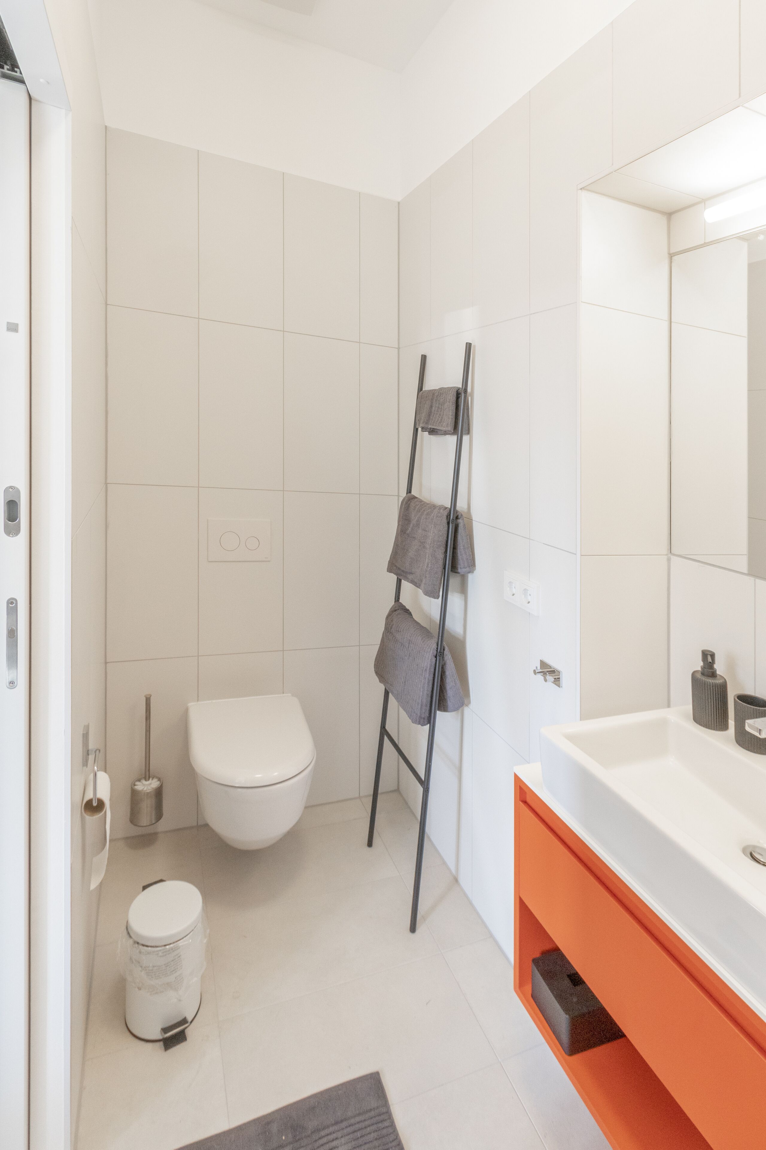 A modern bathroom with a white toilet, a sink with an orange vanity, and a towel rack.