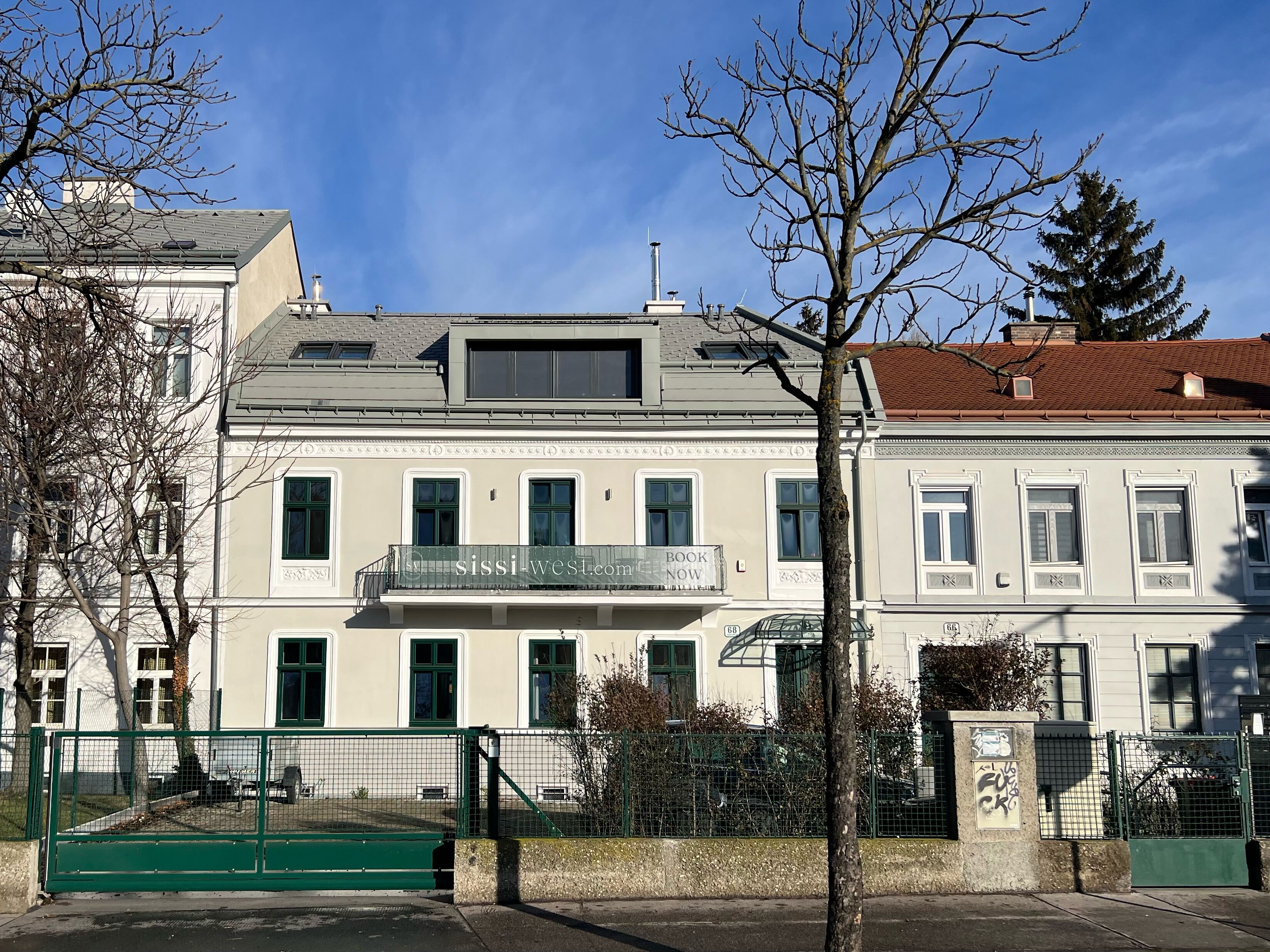 A two-story building with a balcony, a gated entrance, and a clear sky.