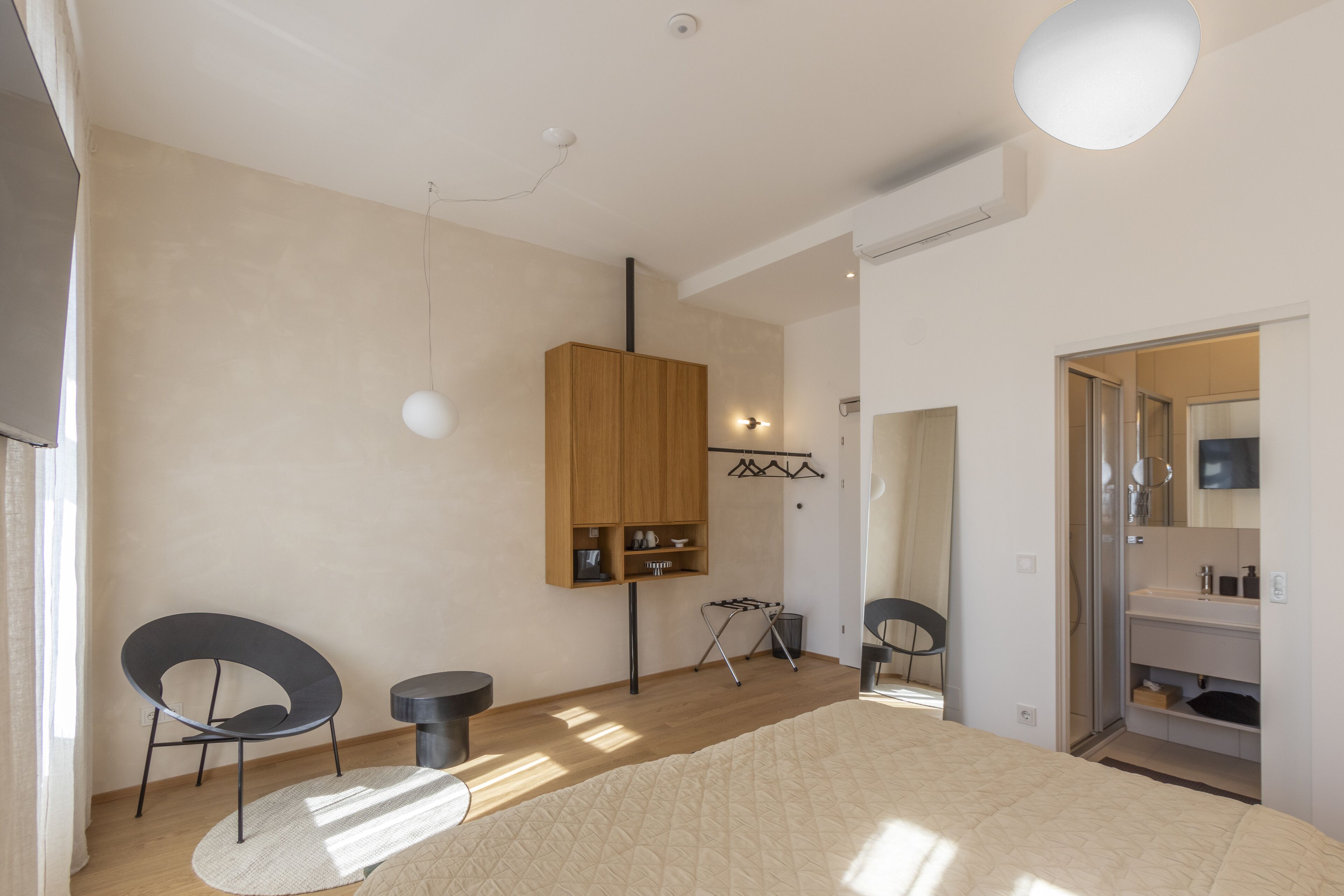 A modern bedroom with a bed, two chairs, a wooden wardrobe, a small table, and a mirror.