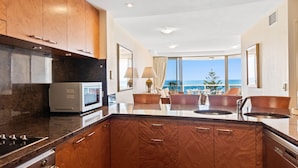 Una cocina moderna con vista al océano, armarios de madera, microondas integrado y un comedor con vista.