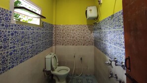 Een compacte badkamer met gele wanden, een toilet, een douche en een raam met uitzicht op groen.