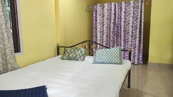 A single bed with two pillows, a window with a curtain, and a shower curtain with a leaf pattern.