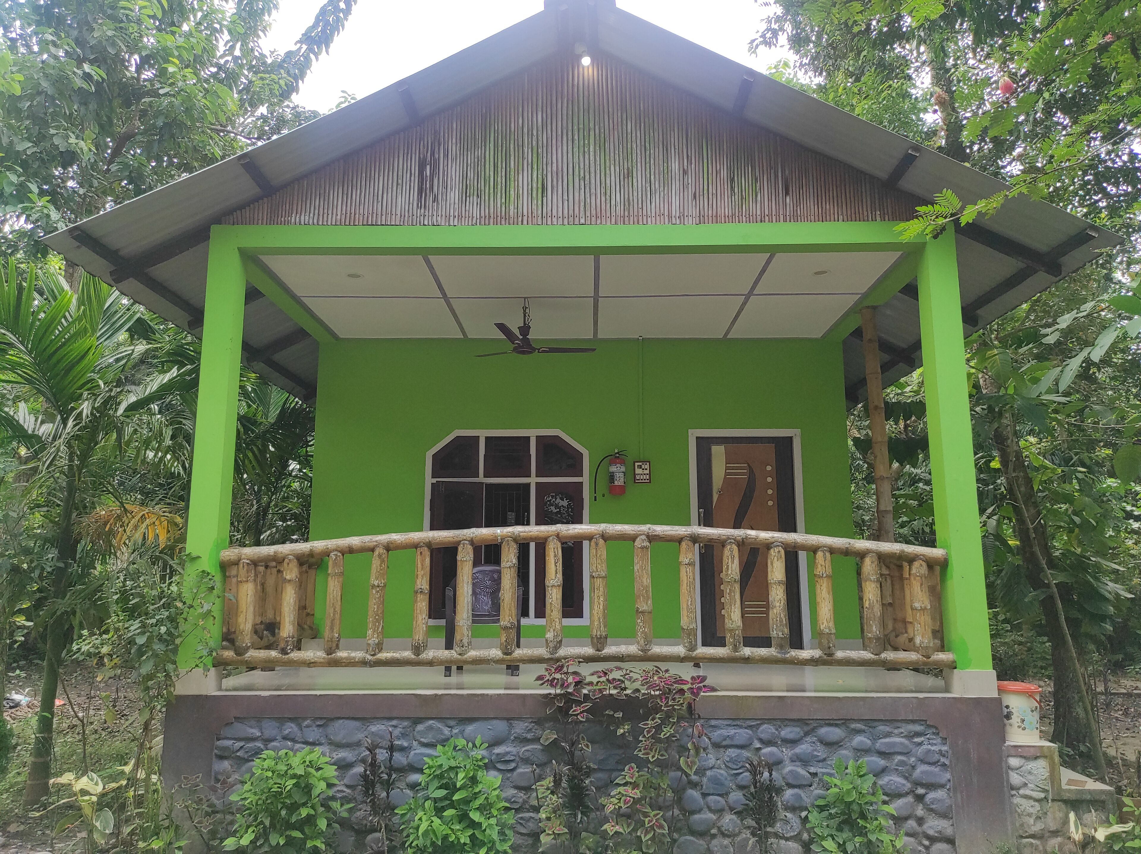Een gebouw in groene tinten met een overdekte veranda, een deur en een raam.