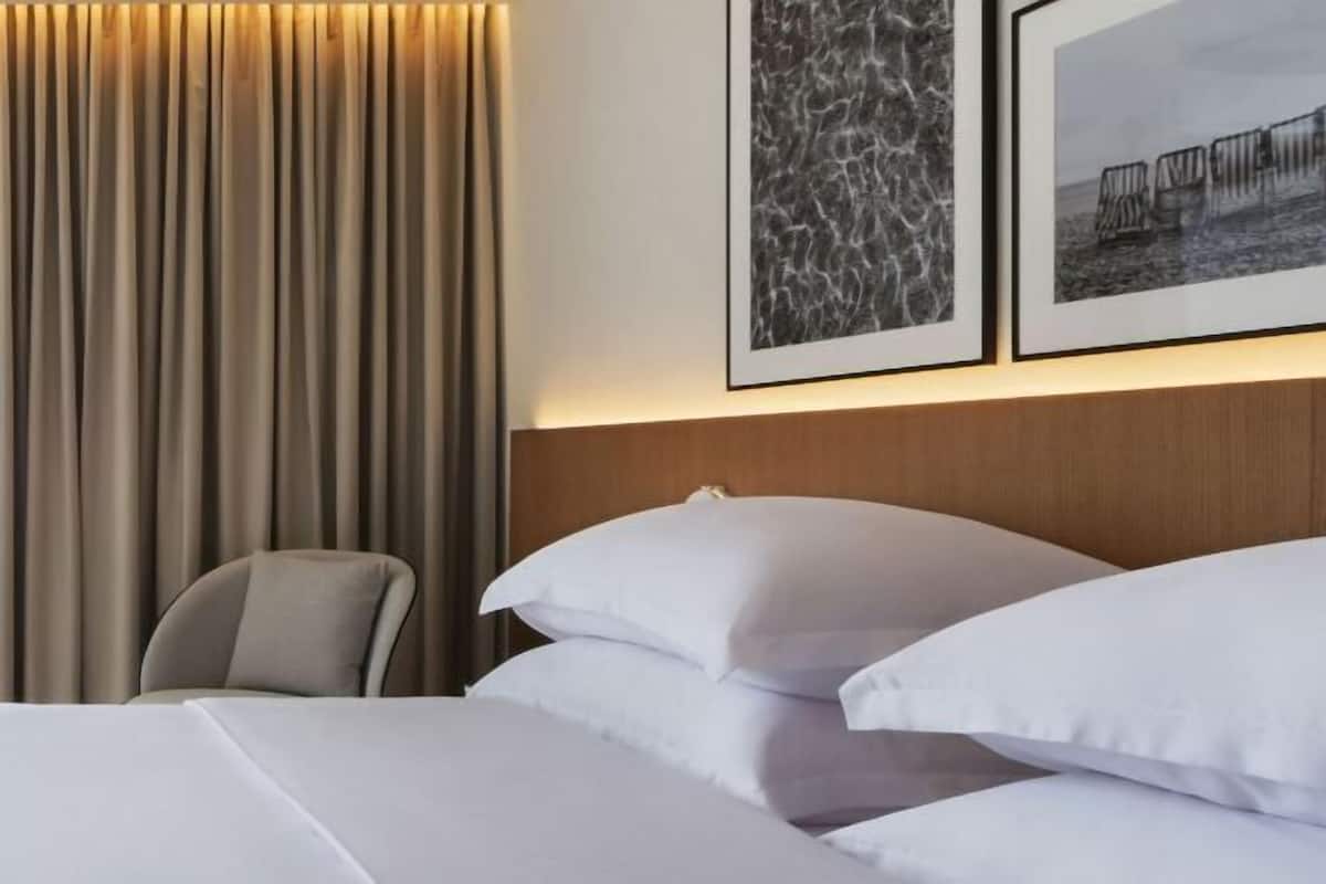 Une chambre d’hôtel avec un lit, des oreillers, une chaise et deux tableaux encadrés au mur.