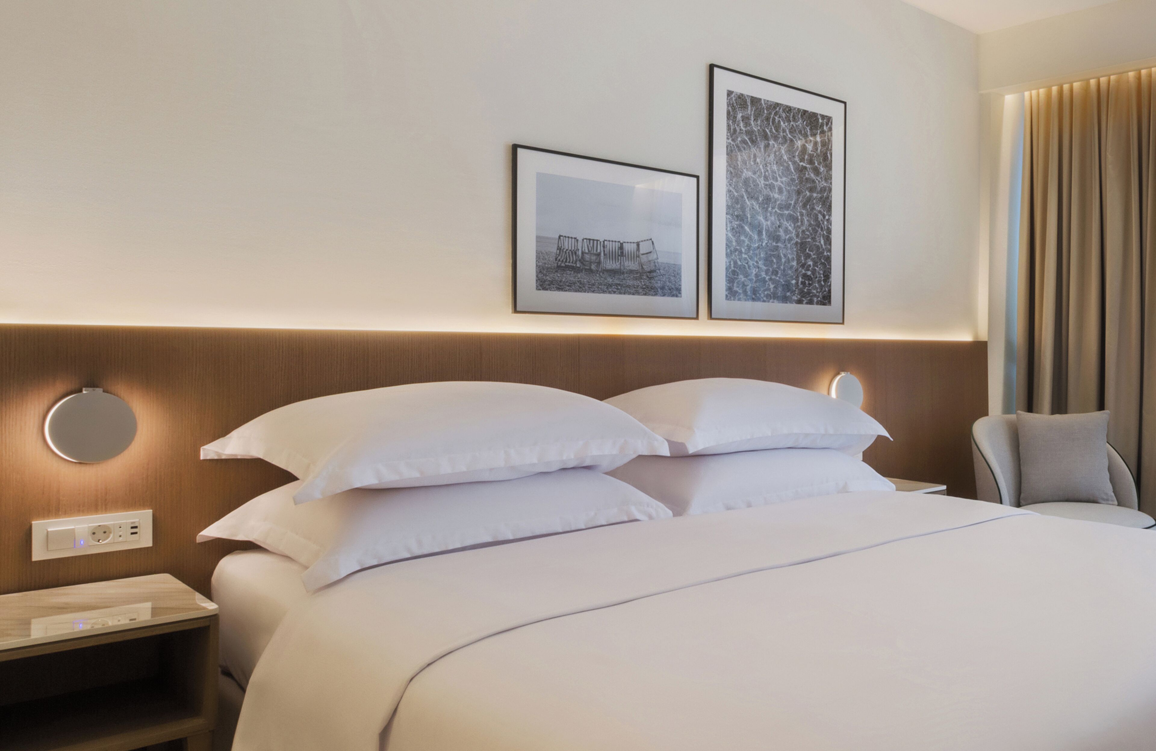 A neatly made bed with white linens, a bedside table with a lamp, and two framed pictures on the wall.