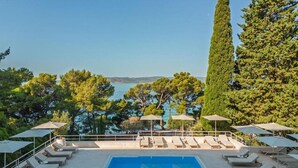 A poolside area with lounge chairs and umbrellas, overlooking a body of water and trees. - Maestral Adults Exclusive Hotel (Brela)