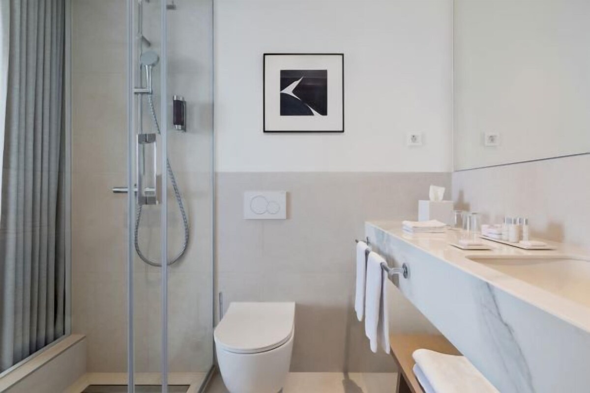 Un baño moderno con cabina de ducha de vidrio, inodoro, lavamanos con encimera de mármol y un cuadro enmarcado en la pared.