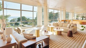 A spacious living room with large windows, a sofa set, coffee tables, and a view of the sea. - Maestral Adults Exclusive Hotel (Brela)