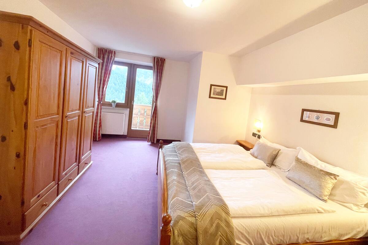 Un dormitorio con dos camas, un armario de madera, una ventana con cortinas y un radiador.