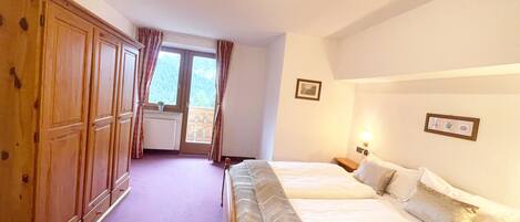 A bedroom with two beds, wooden wardrobe, a window with curtains, and a radiator.