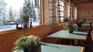 A restaurant with wooden interior, large windows, and tables with green tablecloths. - PLOSE Parkhotel & Residence (Bressanone)