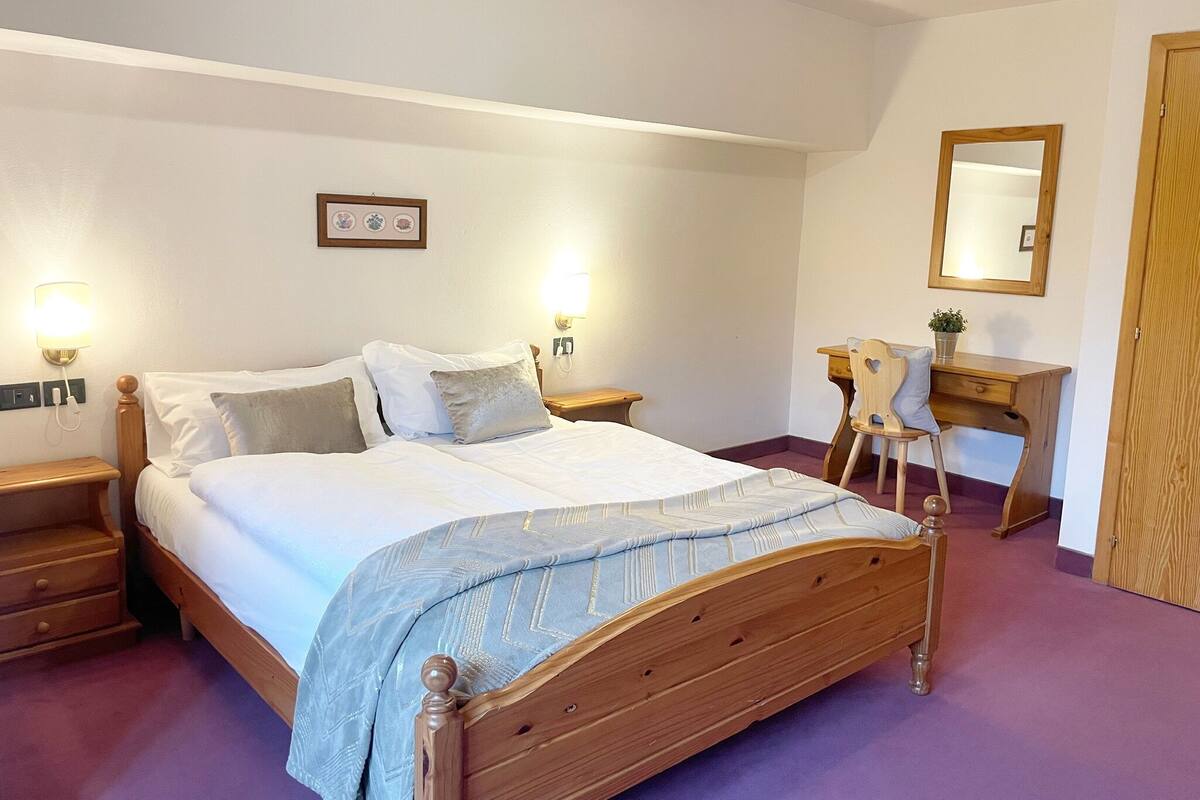 Un dormitorio con cama de madera, mesitas de noche, un escritorio, una silla, un espejo y un teléfono instalado en la pared.