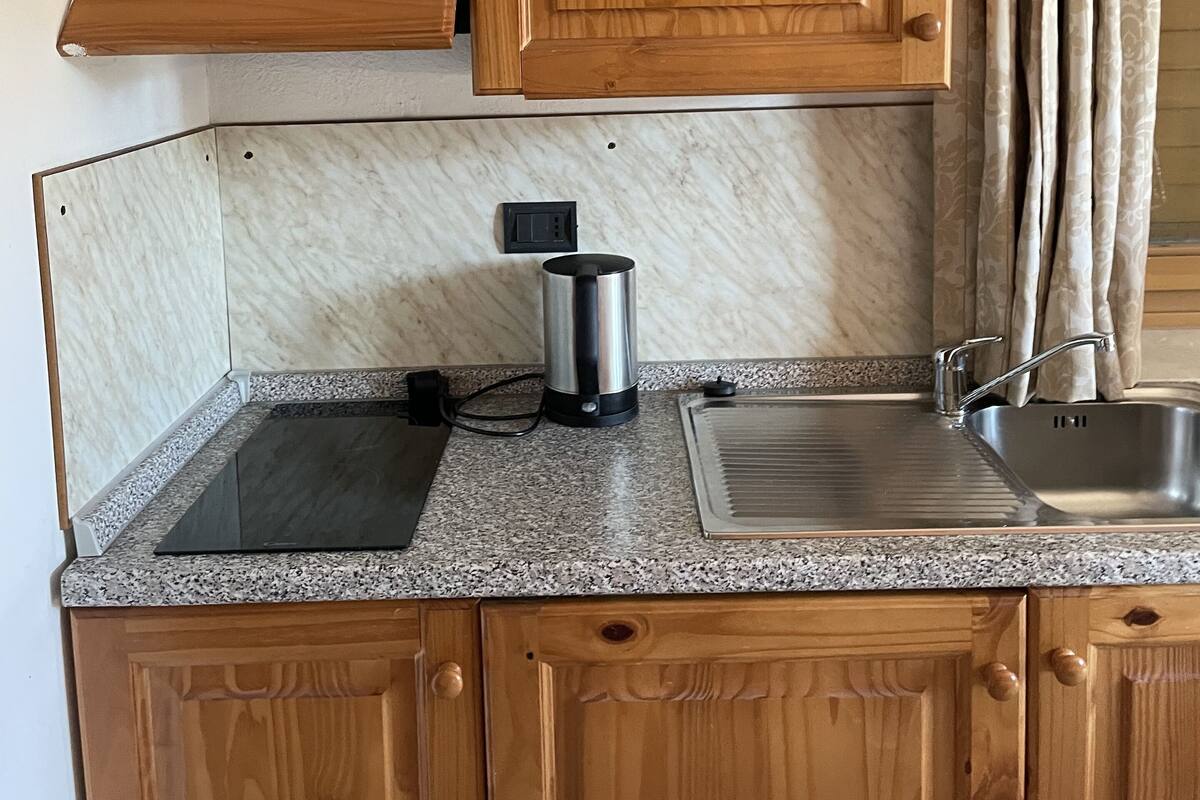 Una cocina con armarios de madera, encimera de granito, pileta de acero inoxidable y cafetera.