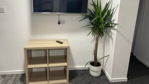 A room with a mounted TV, a small wooden shelf with a remote, and a potted plant. - Modern and Cosy Apartment in Leeds, England (Leeds)