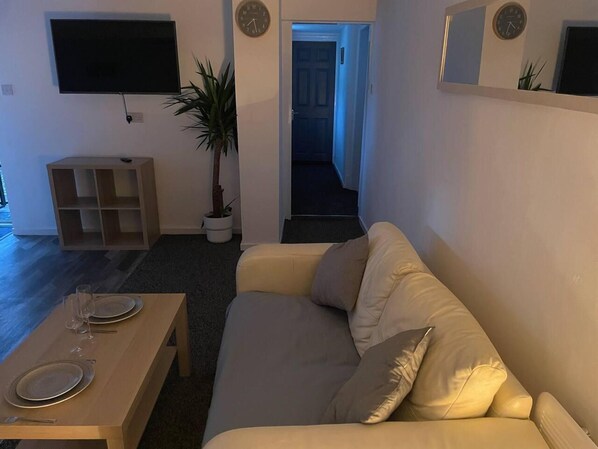 A living room with a sofa, a coffee table, a TV mounted on the wall, a small wooden cabinet, and a potted plant. - Modern and Cosy Apartment in Leeds, England (Leeds)