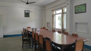 A conference room with a long table, chairs, a ceiling fan, windows, and a framed picture on the wall. - Homecation Manas View Jungle Resort (Barnagar)