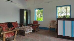 A room with a wooden sofa, a small table with a lace tablecloth, a cabinet, and a window with a view of greenery. - Homecation Manas View Jungle Resort (Barnagar)