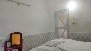 A small, sparsely furnished room with a single bed, a chair, and a door. - Homecation Manas View Jungle Resort (Barnagar)