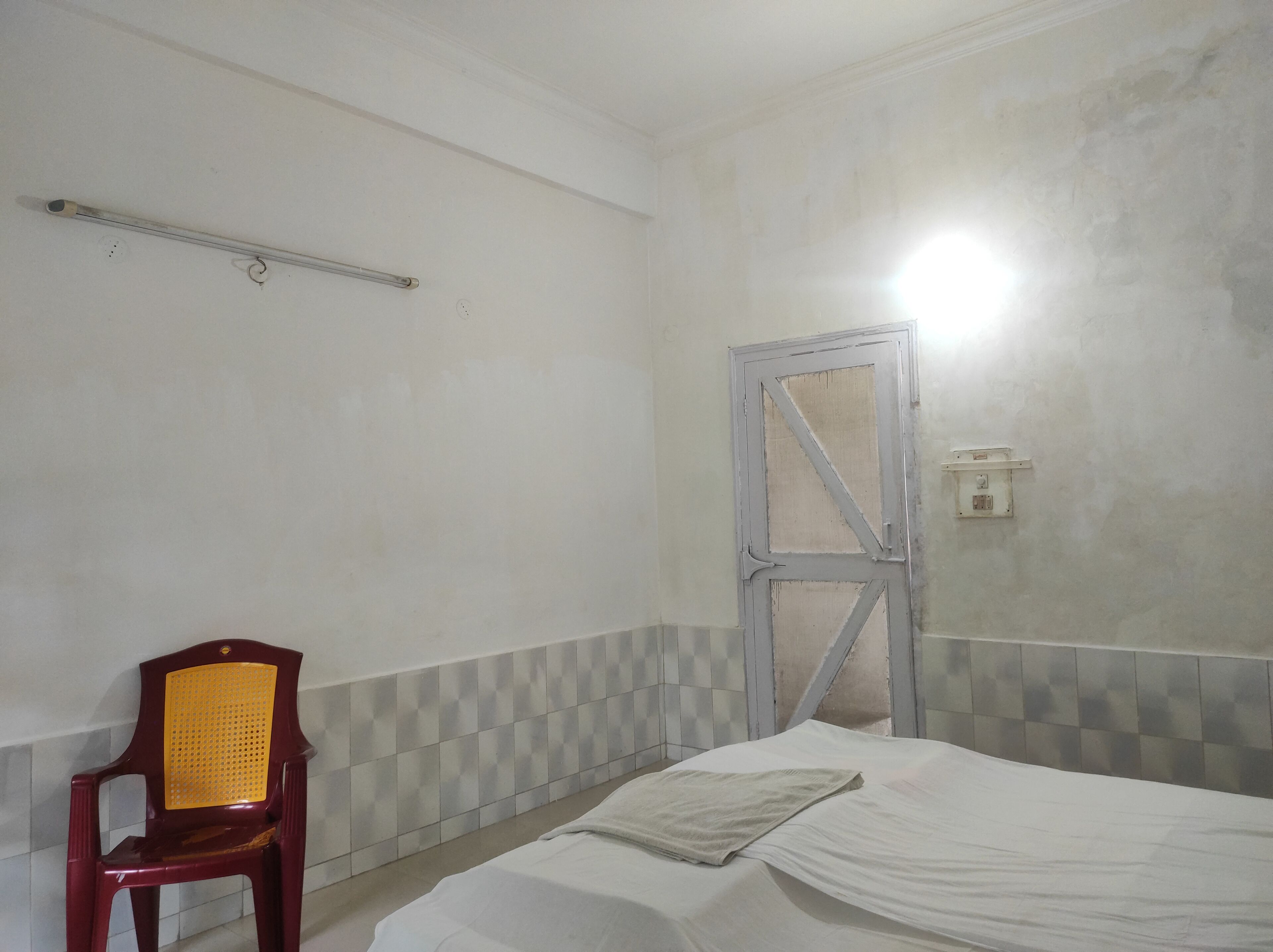 A room with a bed, a chair, a door, and a light fixture.