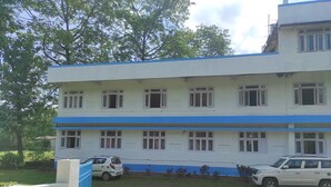 A multi-story building with a blue and white facade, multiple windows, and a parking area with two cars. - Homecation Manas View Jungle Resort (Barnagar)