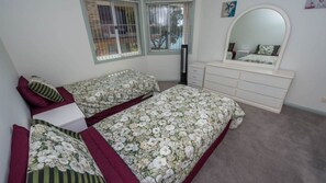 Two single beds with floral-patterned bedding, a dresser and large mirror.