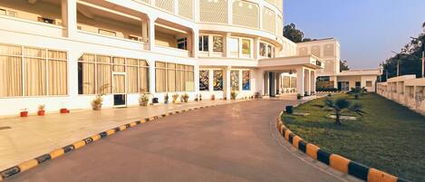 A large, multi-story building with a curved facade, multiple balconies, and a central courtyard with potted plants.
