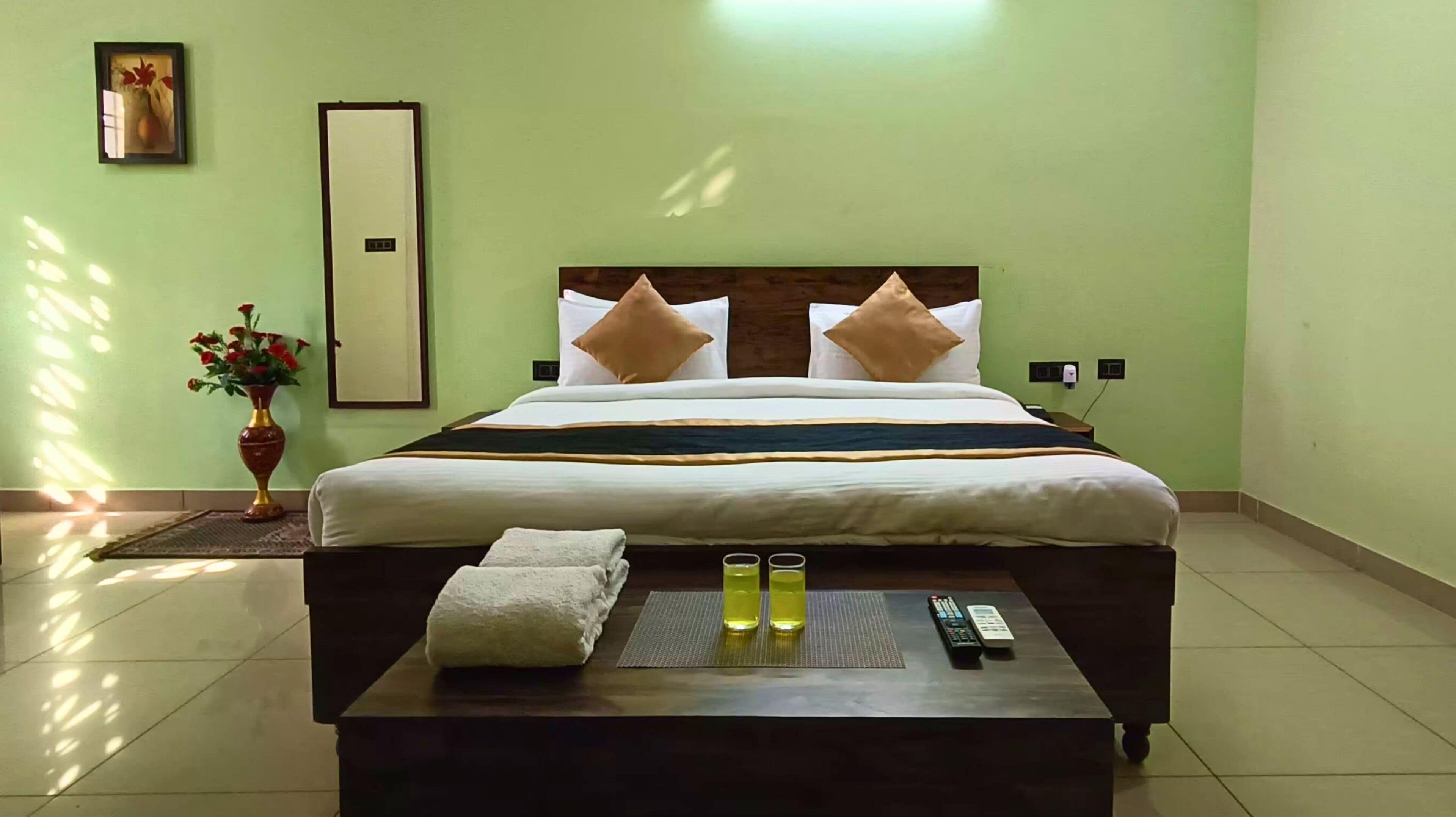 A hotel room with a bed, a bedside table with a remote control, and a vase with flowers.