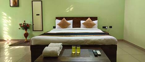 A hotel room with a bed, a bedside table with a remote control, and a vase with flowers.